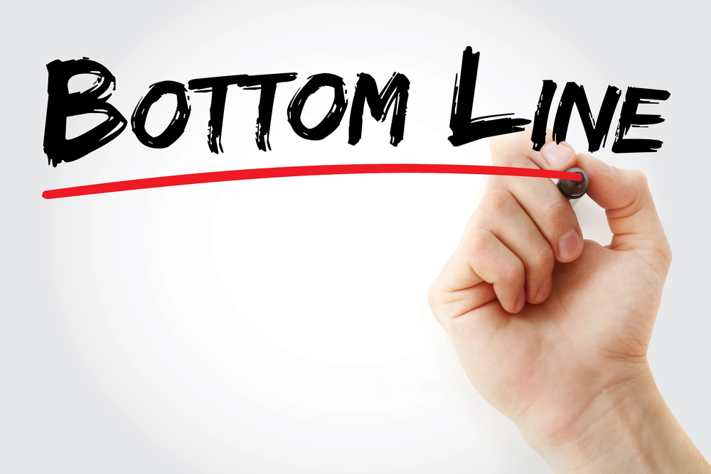 A hand is writing the words, bottom Line, on a whiteboard.   