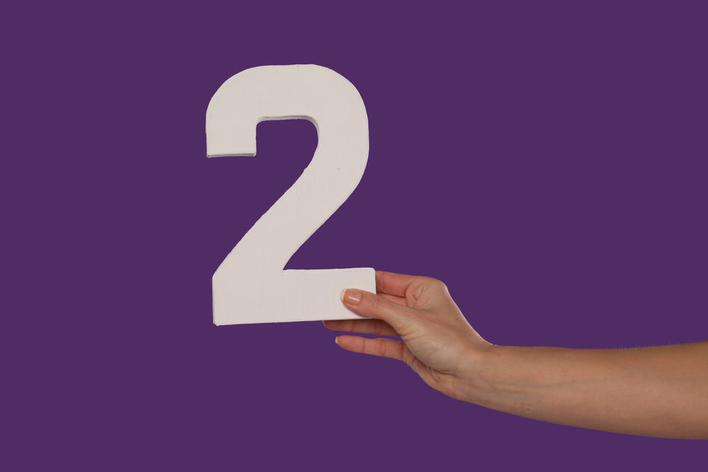 A person is holding a number 2 sign against a purple background.