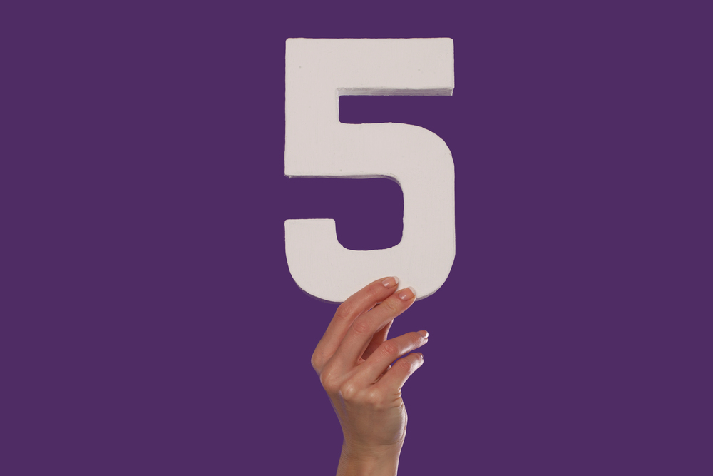 A person is holding the number 5 against a purple background.