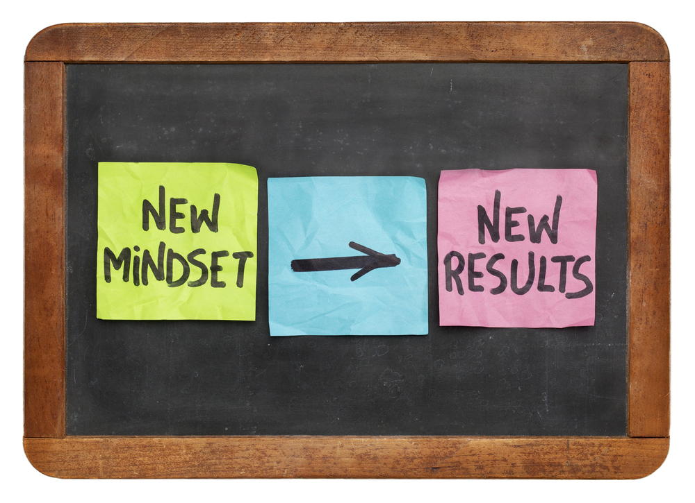 Three sticky notes are on a blackboard. The first sticky note reads, New Mindset. The second sticky note has an arrow pointing to the third sticky note which reads new results.