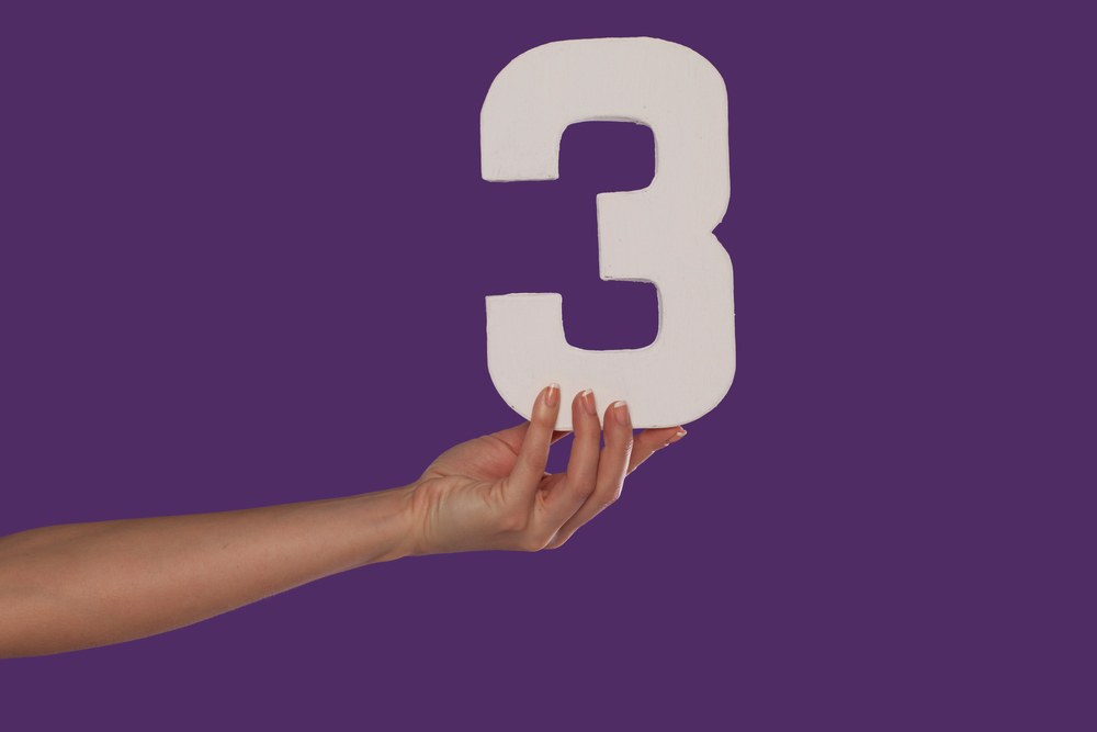 Person is holding the number 3 sign against a purple background.
