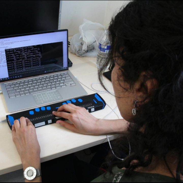 AI and assistive technology work together.  A woman is using a braille device with a laptop.