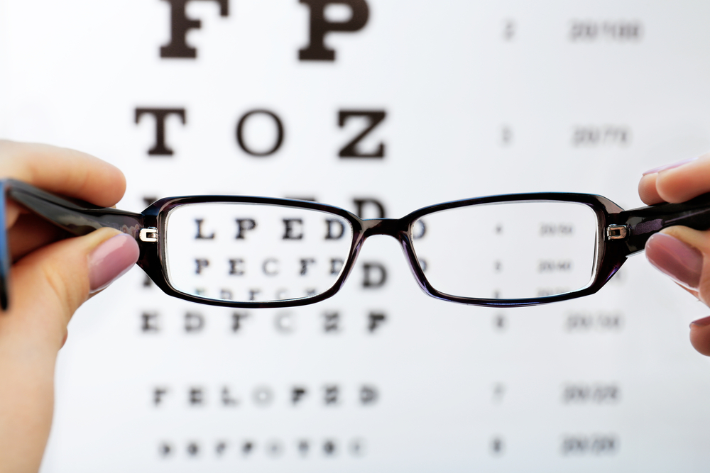 Eye glasses in female hands on eyesight test chart background