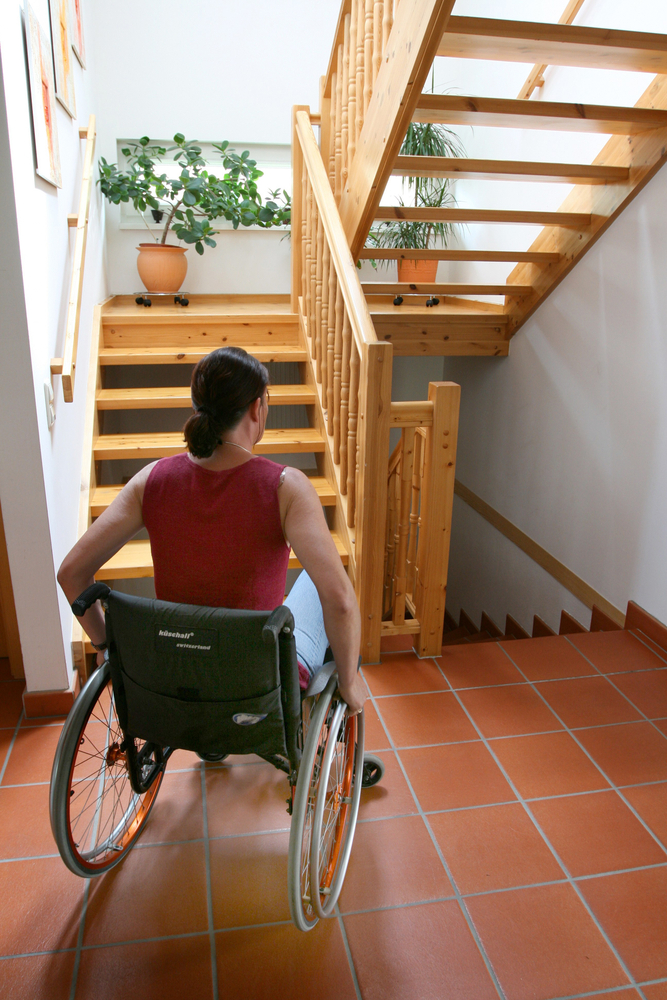 A woman in a wheelchair at the bottom of a staircase.