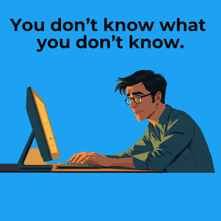 A man is sitting at a desk and looking at a computer. He is looking confused.