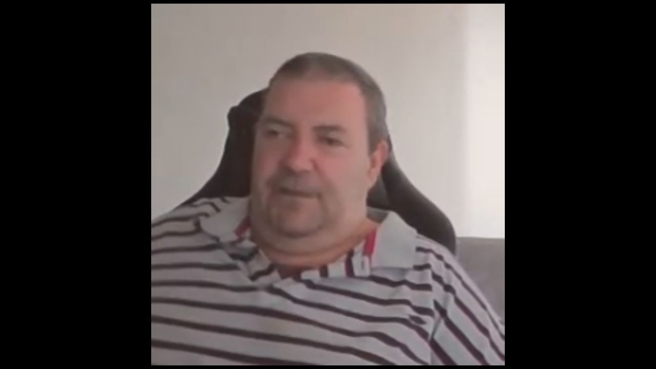 Aaron Orme is wearing a striped polo shirt and sitting on a chair.