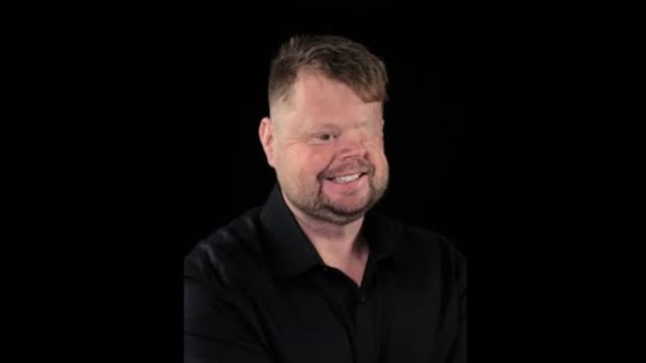 Craig Shanahan is wearing a black shirt and standing against a black wall.