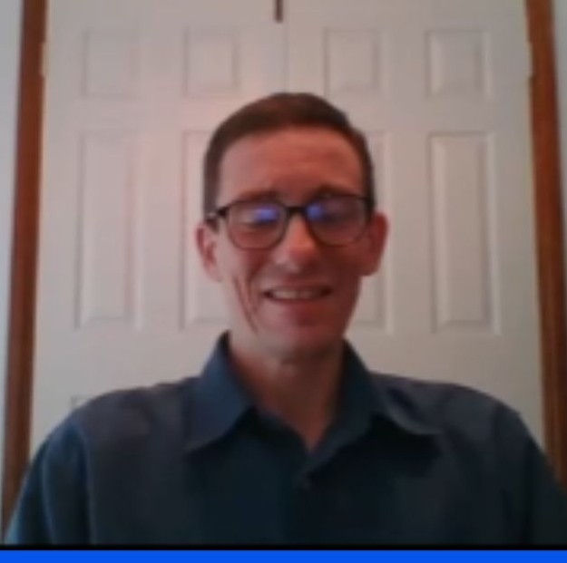 David Oram is sitting and smiling at the camera.